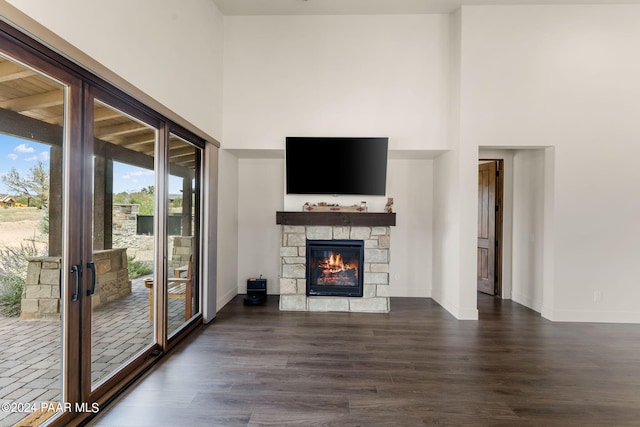 unfurnished living room with a stone fireplace, french doors, a towering ceiling, and dark hardwood / wood-style floors