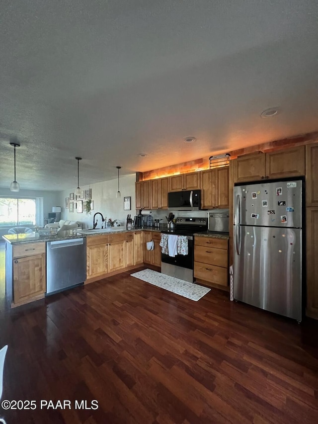 kitchen with appliances with stainless steel finishes, dark wood-type flooring, kitchen peninsula, and decorative light fixtures