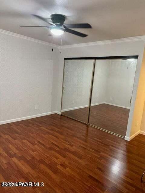 unfurnished bedroom with crown molding, ceiling fan, dark hardwood / wood-style flooring, and a closet