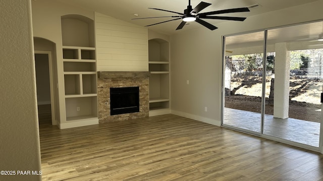 unfurnished living room with hardwood / wood-style floors, ceiling fan, built in features, and a stone fireplace