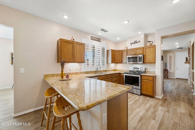 kitchen with visible vents, a peninsula, brown cabinetry, stainless steel appliances, and a sink