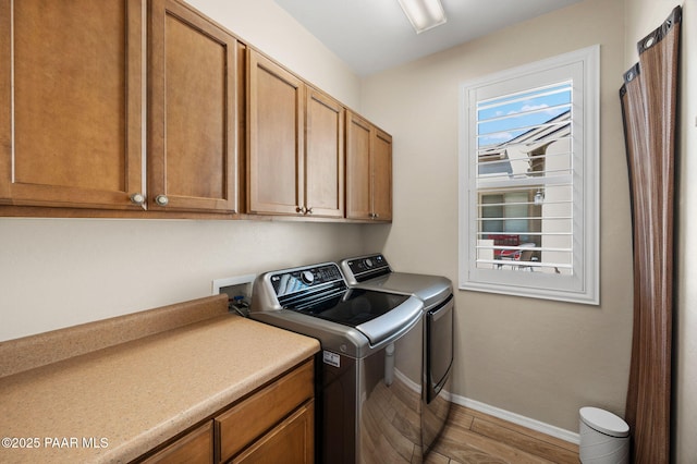 washroom featuring baseboards, cabinet space, light wood-style floors, and independent washer and dryer