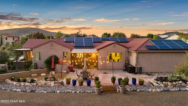 view of front facade with a patio area, stucco siding, solar panels, and a tile roof