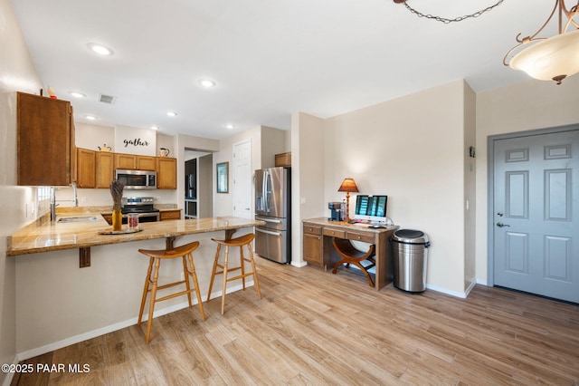 kitchen featuring light wood finished floors, brown cabinets, appliances with stainless steel finishes, a peninsula, and a sink