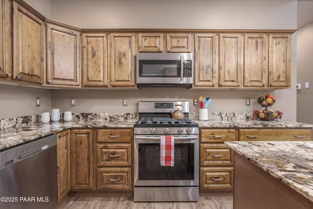 kitchen featuring stainless steel appliances, light stone countertops, brown cabinets, and light wood-style flooring