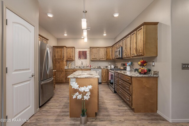 kitchen with brown cabinetry, appliances with stainless steel finishes, a center island, and light stone countertops