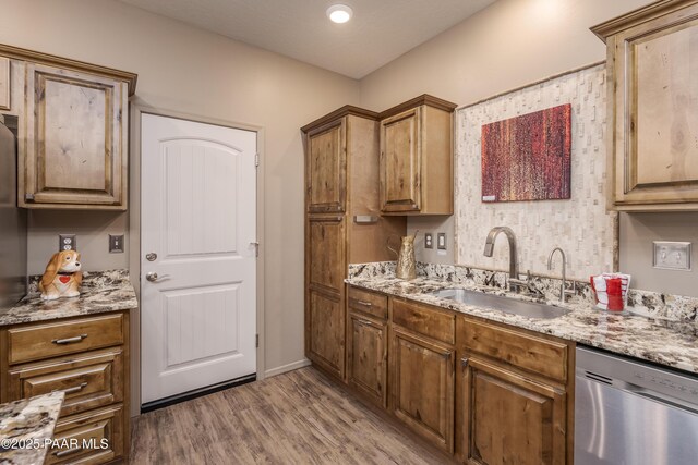 kitchen featuring a sink, light stone countertops, stainless steel dishwasher, and wood finished floors