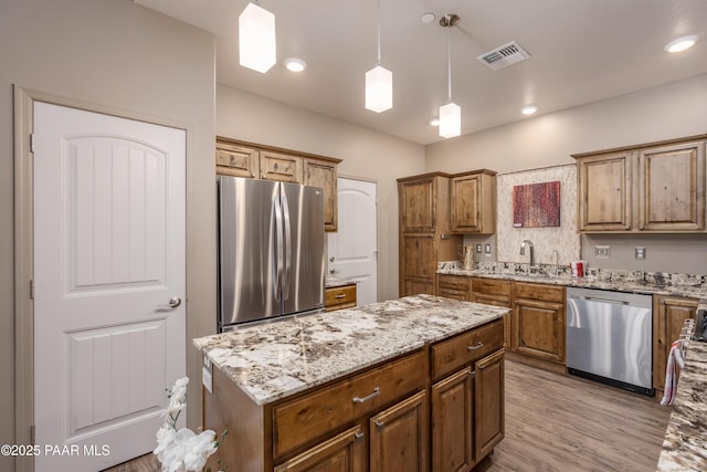 kitchen with light wood-type flooring, visible vents, stainless steel appliances, light stone countertops, and hanging light fixtures