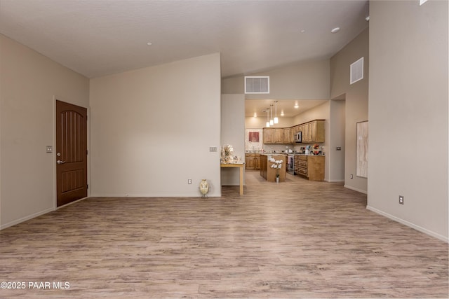 living area with visible vents, light wood-style flooring, high vaulted ceiling, and baseboards