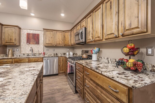 kitchen featuring light stone countertops, light wood-style floors, appliances with stainless steel finishes, and a sink