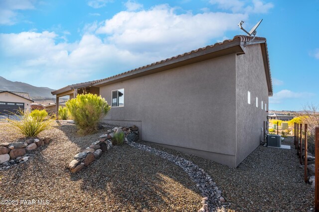 view of home's exterior featuring central AC unit, stucco siding, a mountain view, and fence