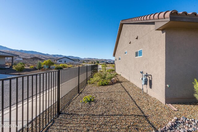 view of property exterior featuring a tiled roof, stucco siding, a mountain view, and fence