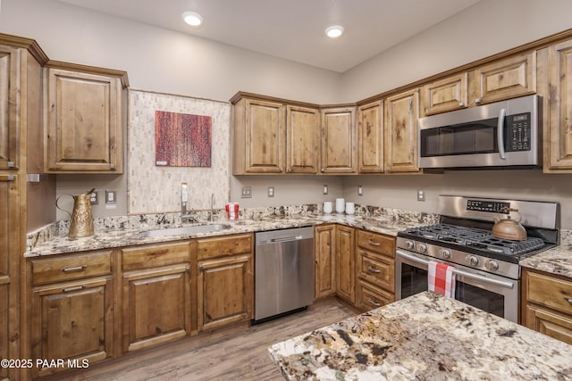 kitchen with light stone counters, brown cabinets, appliances with stainless steel finishes, and light wood-style flooring