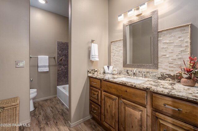 bathroom with toilet, a tub to relax in, wood finished floors, baseboards, and vanity