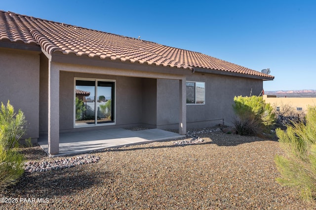 back of house with stucco siding, a tiled roof, and a patio