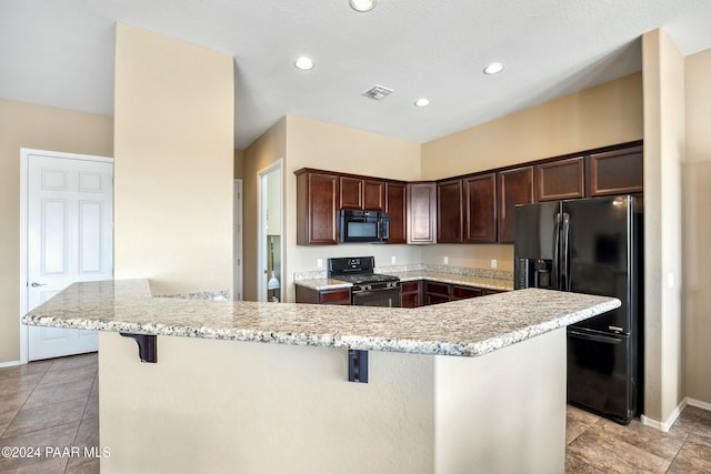 kitchen featuring light stone counters, dark brown cabinetry, black appliances, a center island, and a breakfast bar area