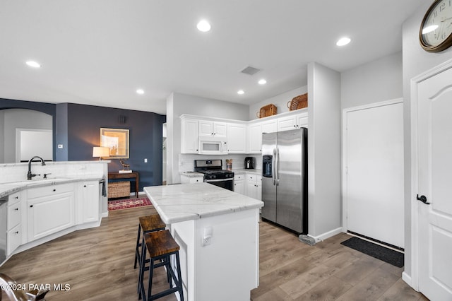 kitchen featuring white cabinetry, sink, stainless steel appliances, light hardwood / wood-style flooring, and a kitchen island