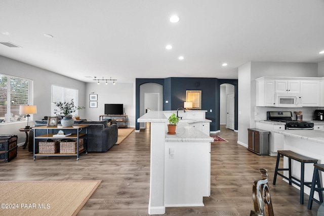 kitchen with a kitchen island with sink, white cabinets, a kitchen breakfast bar, gas range, and hardwood / wood-style flooring