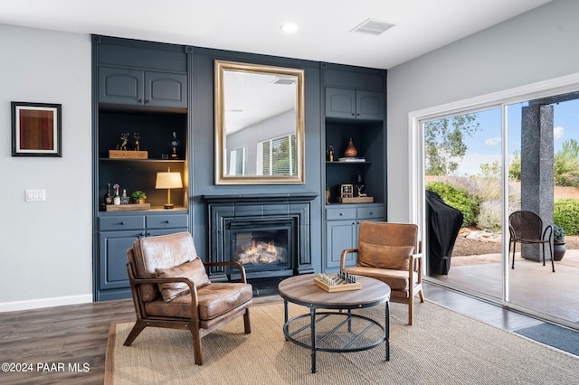 living area with built in shelves, a large fireplace, and hardwood / wood-style flooring