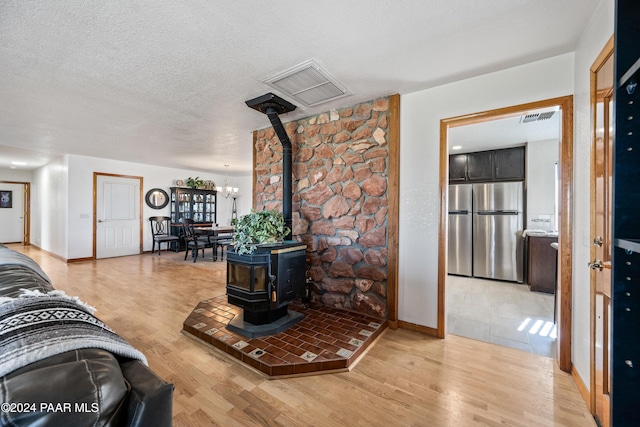 living room featuring a wood stove, a chandelier, a textured ceiling, and hardwood / wood-style flooring