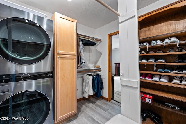 laundry area with cabinets, a textured ceiling, light hardwood / wood-style flooring, and stacked washer / dryer