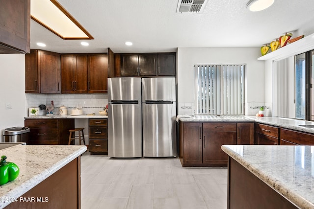 kitchen with stainless steel refrigerator, light stone countertops, a textured ceiling, decorative backsplash, and dark brown cabinets