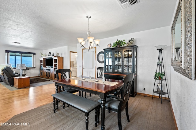 dining area featuring wood-type flooring, a textured ceiling, and an inviting chandelier