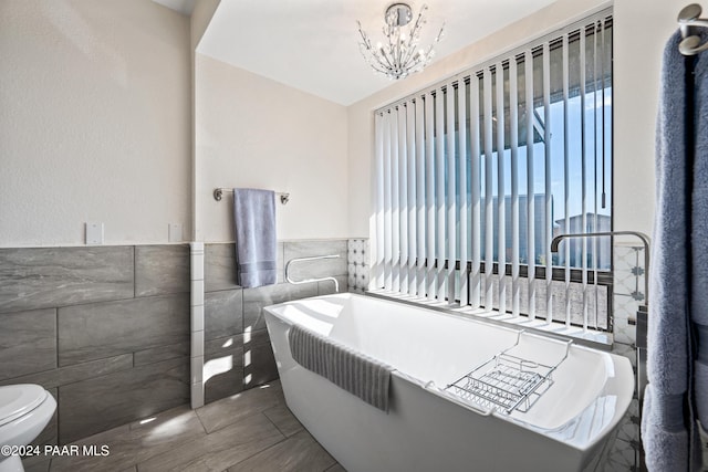 bathroom with a chandelier, a bath, toilet, and tile walls