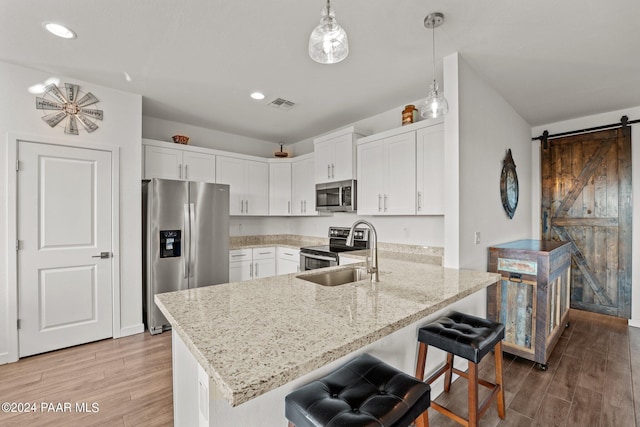 kitchen with white cabinets, a barn door, decorative light fixtures, light hardwood / wood-style floors, and stainless steel appliances