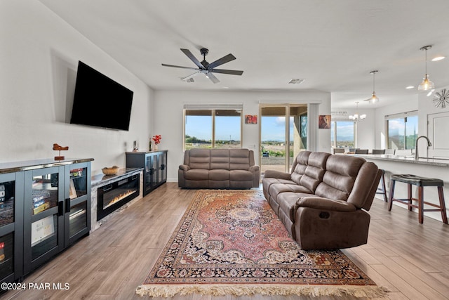 living room featuring sink, light hardwood / wood-style floors, and ceiling fan with notable chandelier