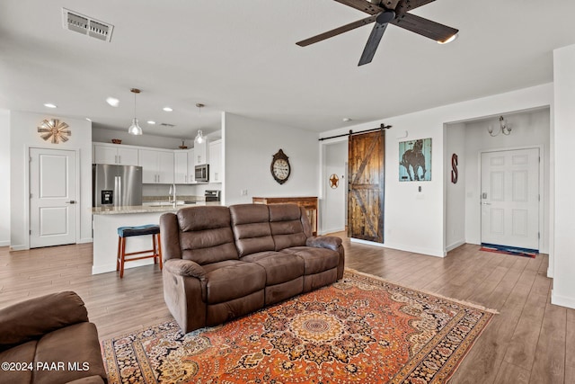 living room with ceiling fan, a barn door, light wood-type flooring, and sink