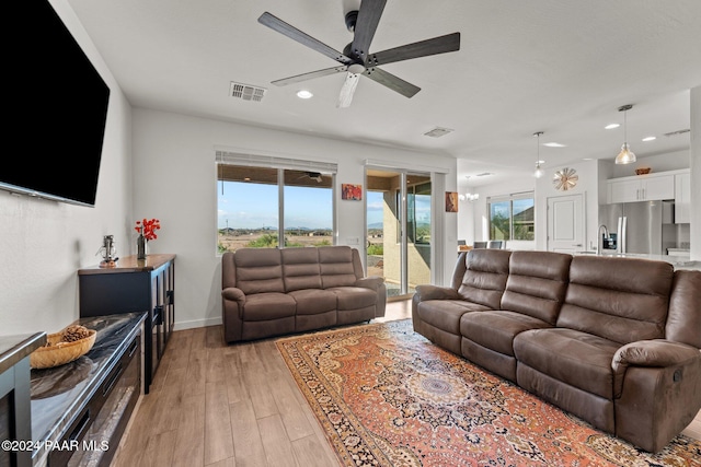 living room featuring ceiling fan with notable chandelier, sink, and light hardwood / wood-style flooring