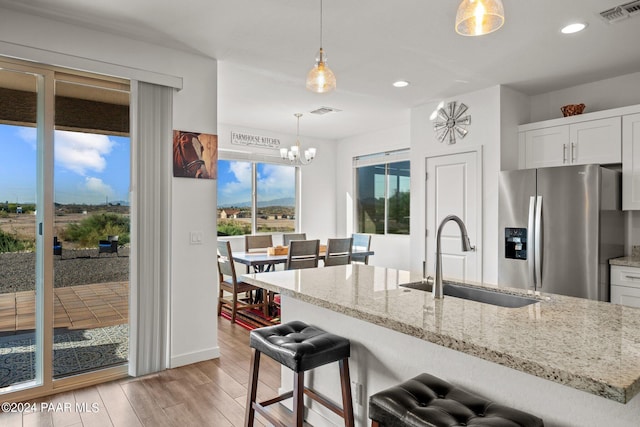 kitchen with sink, stainless steel refrigerator with ice dispenser, hanging light fixtures, light wood-type flooring, and white cabinetry