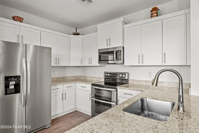 kitchen featuring appliances with stainless steel finishes, light stone counters, sink, hardwood / wood-style floors, and white cabinetry