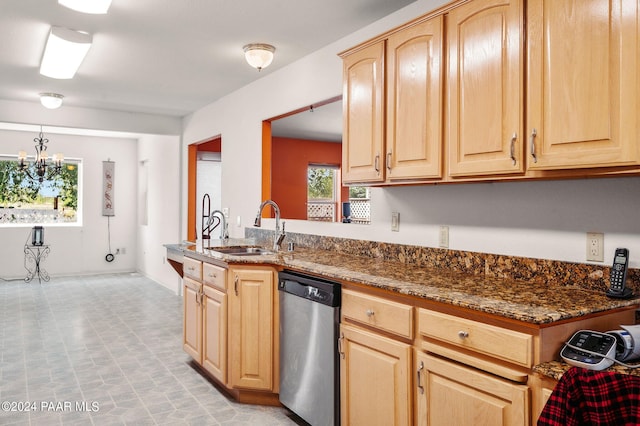 kitchen with stainless steel dishwasher, sink, light brown cabinets, a notable chandelier, and dark stone countertops