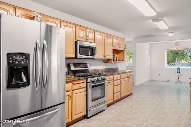 kitchen with dark stone countertops, light brown cabinets, stainless steel appliances, and an inviting chandelier