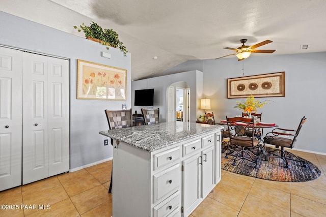 kitchen featuring light tile patterned floors, a breakfast bar area, white cabinetry, light stone countertops, and a kitchen island