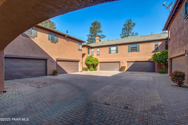 view of front facade featuring a garage, stucco siding, a chimney, and driveway