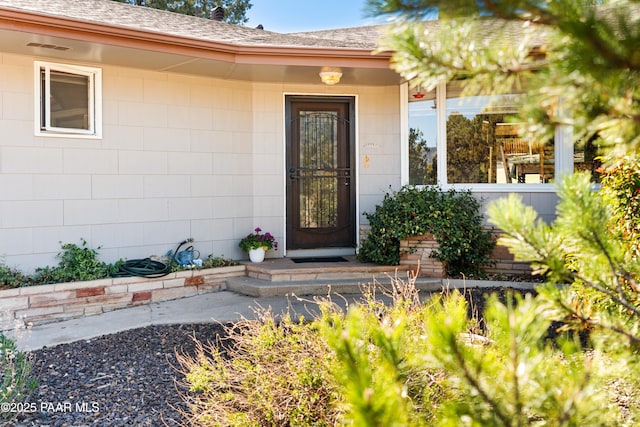 entrance to property featuring covered porch and roof with shingles