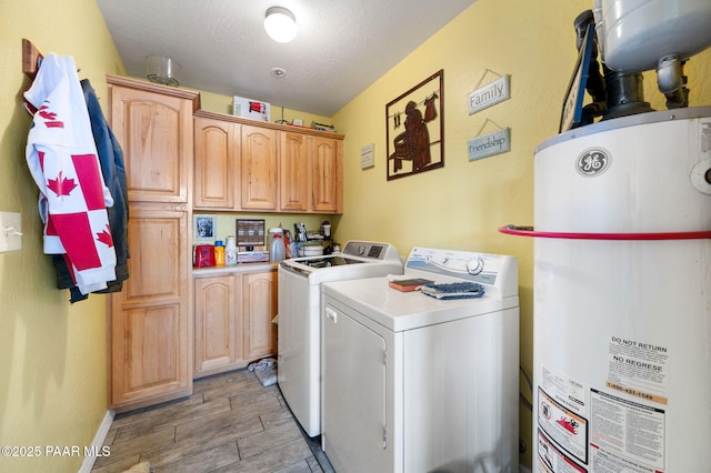 clothes washing area with cabinet space, washing machine and clothes dryer, wood tiled floor, a textured ceiling, and gas water heater