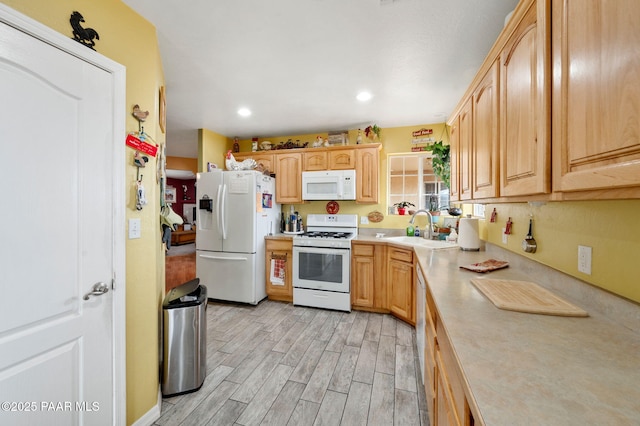 kitchen with white appliances, light countertops, light brown cabinetry, light wood-type flooring, and a sink