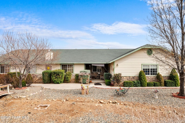 ranch-style home with stone siding, a shingled roof, and a patio