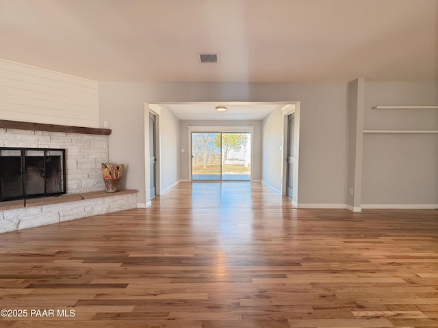 unfurnished living room featuring hardwood / wood-style flooring and a stone fireplace