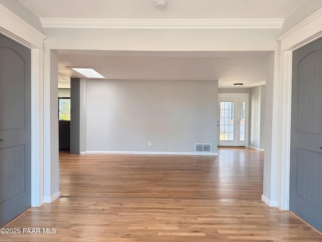 empty room with crown molding, plenty of natural light, a skylight, and light hardwood / wood-style flooring