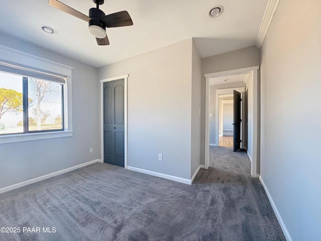 unfurnished bedroom with crown molding, ceiling fan, dark carpet, and a closet