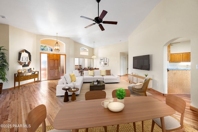 living room with ceiling fan with notable chandelier, high vaulted ceiling, and light hardwood / wood-style floors
