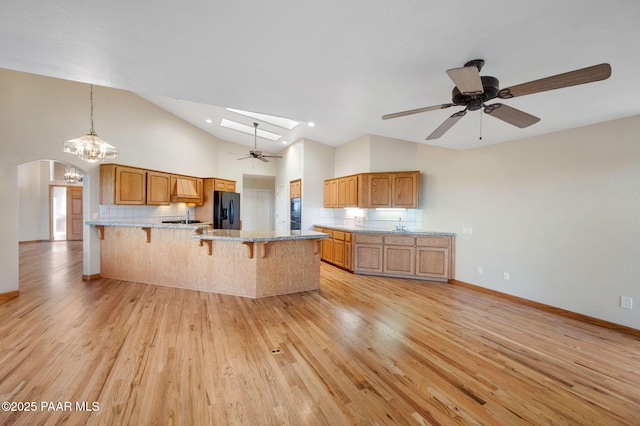 kitchen with tasteful backsplash, black fridge with ice dispenser, light hardwood / wood-style flooring, and a breakfast bar