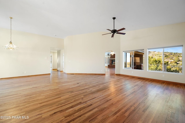 unfurnished living room with ceiling fan with notable chandelier, high vaulted ceiling, and hardwood / wood-style floors