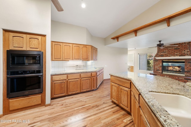 kitchen with sink, black microwave, light stone counters, vaulted ceiling, and stainless steel oven