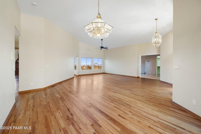 unfurnished living room with ceiling fan with notable chandelier, light hardwood / wood-style flooring, and a high ceiling